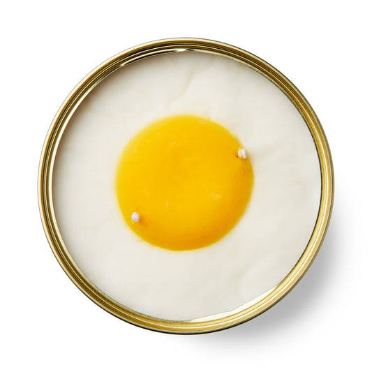 vanilla egg shaped candle in a gold tin on a white background